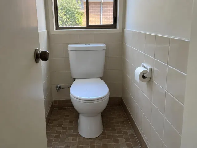 Clean white toilet in a tiled bathroom with a window and toilet paper holder in Glenmore Park
